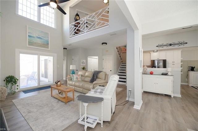 living room with ceiling fan, a healthy amount of sunlight, light hardwood / wood-style floors, and a towering ceiling