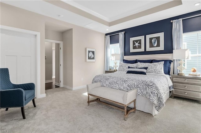 bedroom with light colored carpet, ensuite bath, and a tray ceiling