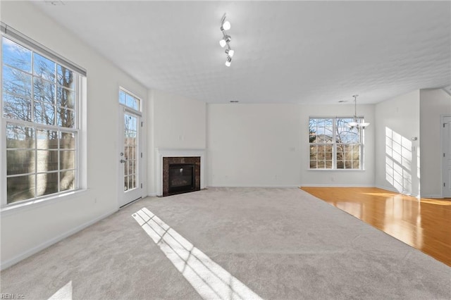 unfurnished living room with an inviting chandelier, light colored carpet, and rail lighting