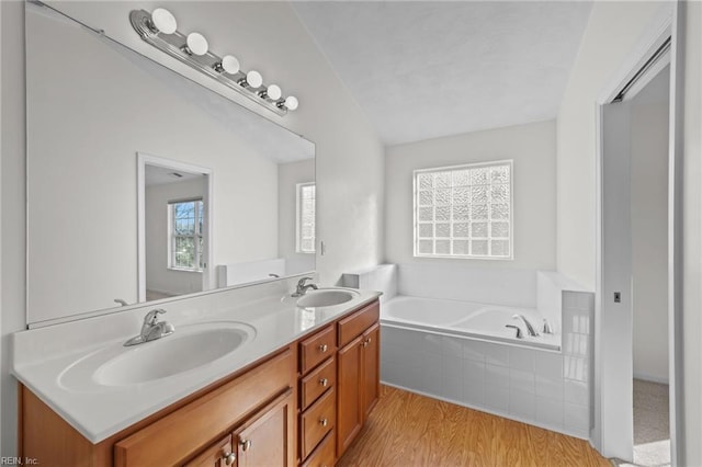 bathroom with hardwood / wood-style flooring, vanity, vaulted ceiling, and tiled tub