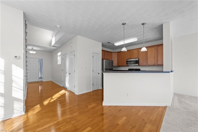 kitchen featuring hanging light fixtures, light hardwood / wood-style flooring, stainless steel appliances, and kitchen peninsula