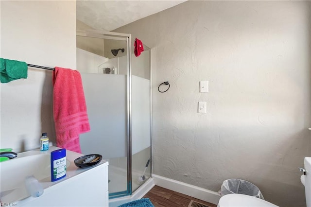 bathroom with wood-type flooring, a shower with door, and toilet