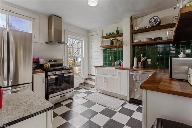 kitchen featuring sink, white cabinetry, butcher block counters, stainless steel appliances, and wall chimney exhaust hood