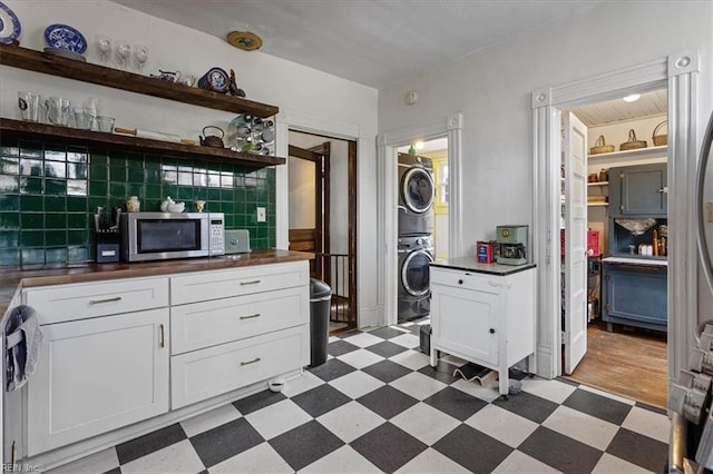 kitchen with white cabinetry, appliances with stainless steel finishes, stacked washing maching and dryer, and backsplash