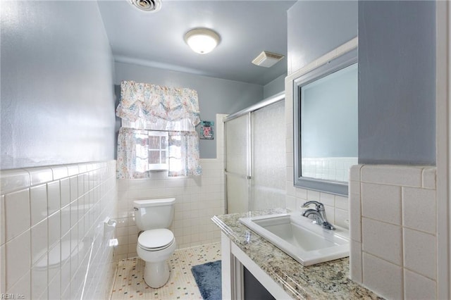 bathroom featuring toilet, a shower with shower door, tile walls, vanity, and tile patterned flooring