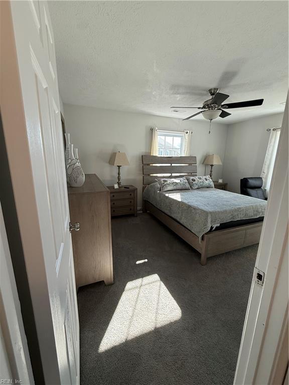 bedroom featuring ceiling fan, dark carpet, and a textured ceiling