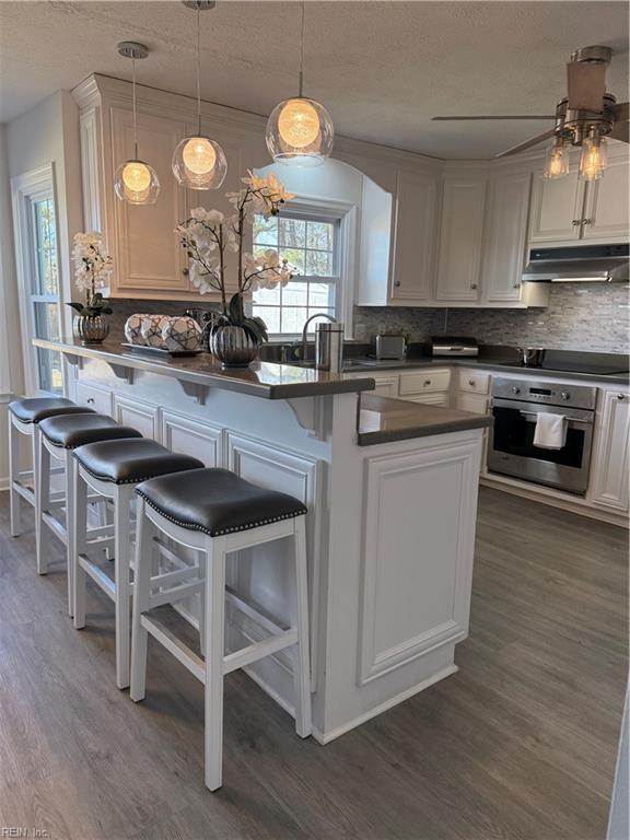 kitchen with pendant lighting, a breakfast bar area, stainless steel oven, and white cabinets