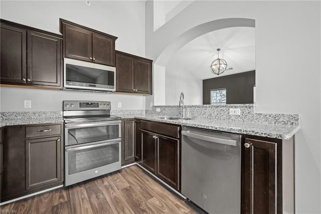 kitchen featuring sink, appliances with stainless steel finishes, dark brown cabinetry, light stone countertops, and dark hardwood / wood-style flooring