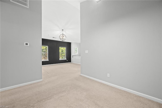 unfurnished living room with a towering ceiling, a chandelier, and light carpet