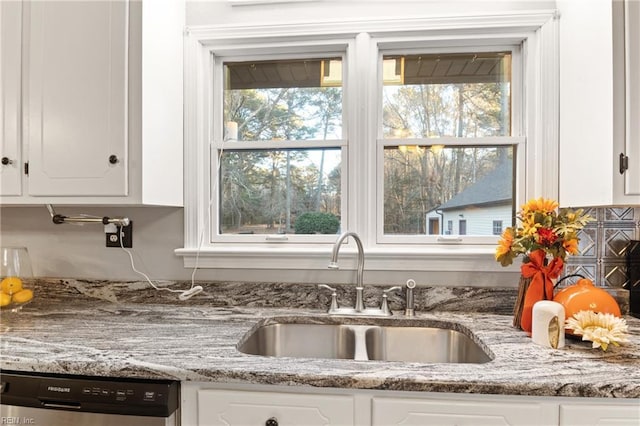 kitchen featuring light stone countertops, sink, stainless steel dishwasher, and white cabinets