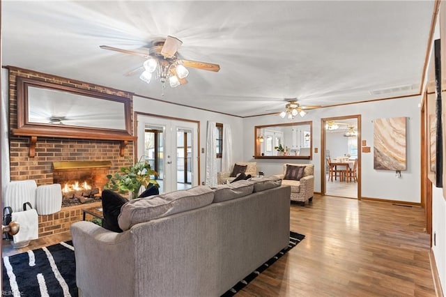 living room featuring french doors, ceiling fan, a fireplace, and light hardwood / wood-style floors