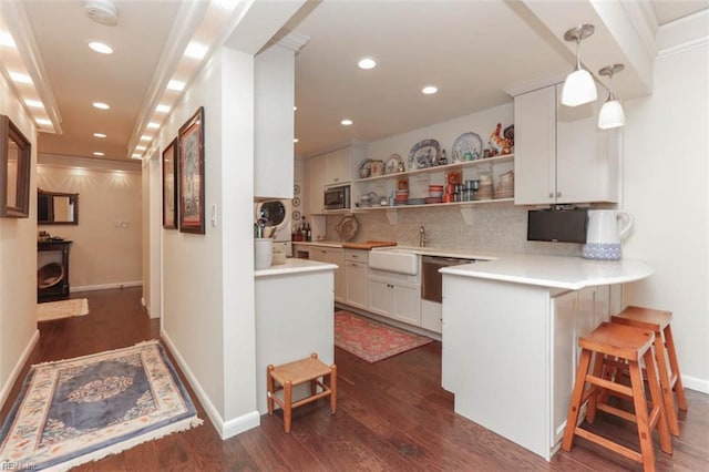 kitchen with pendant lighting, white cabinetry, dark hardwood / wood-style flooring, a kitchen bar, and kitchen peninsula