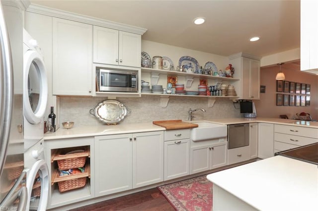 kitchen with stacked washer / drying machine, sink, pendant lighting, stainless steel appliances, and white cabinets