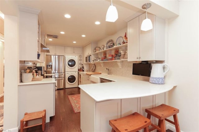 kitchen with stacked washer / drying machine, a kitchen bar, hanging light fixtures, kitchen peninsula, and stainless steel appliances