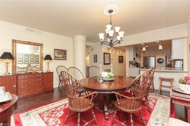 dining room with crown molding, dark hardwood / wood-style floors, stacked washer / drying machine, and an inviting chandelier