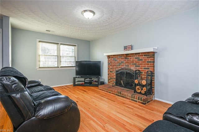 living room featuring hardwood / wood-style flooring, a brick fireplace, and a textured ceiling