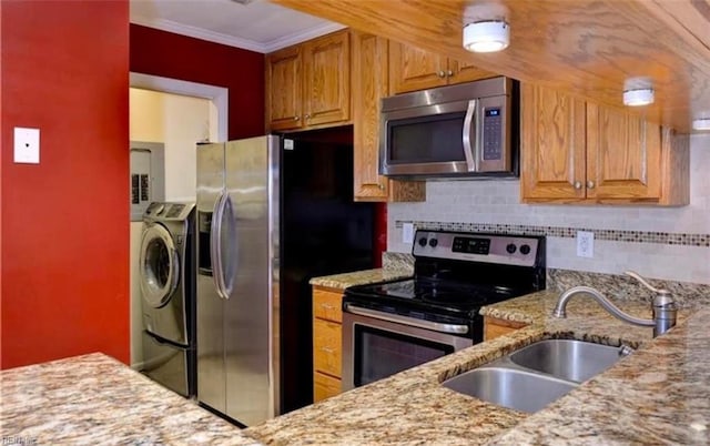 kitchen featuring sink, light stone counters, crown molding, separate washer and dryer, and appliances with stainless steel finishes