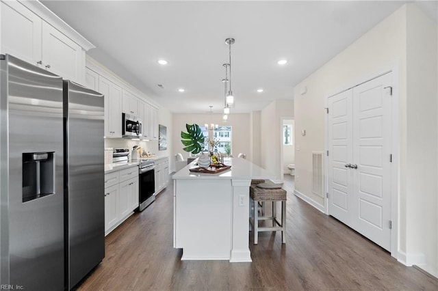 kitchen featuring appliances with stainless steel finishes, white cabinets, a kitchen breakfast bar, hanging light fixtures, and a center island