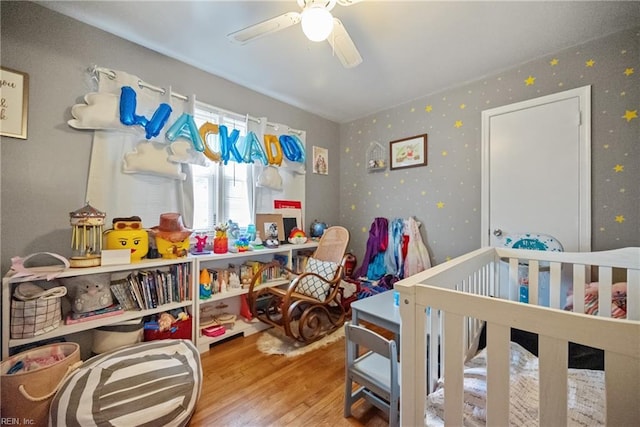 bedroom featuring a crib, hardwood / wood-style floors, and ceiling fan