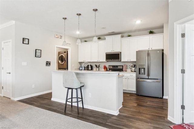 kitchen featuring appliances with stainless steel finishes, pendant lighting, stacked washer / dryer, an island with sink, and white cabinets