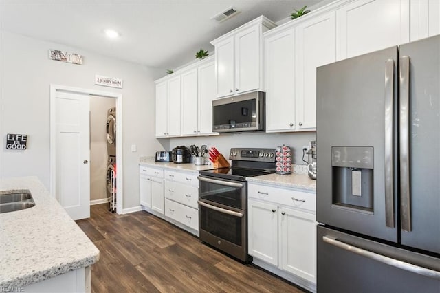 kitchen with dark wood-type flooring, light stone counters, appliances with stainless steel finishes, stacked washing maching and dryer, and white cabinets