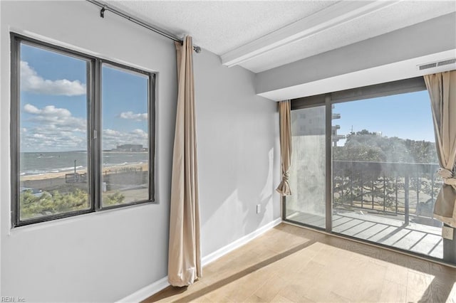 unfurnished room with a water view, a textured ceiling, and light hardwood / wood-style flooring