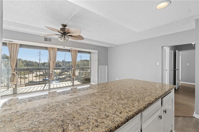 kitchen with white cabinetry, light stone counters, a textured ceiling, hardwood / wood-style flooring, and ceiling fan