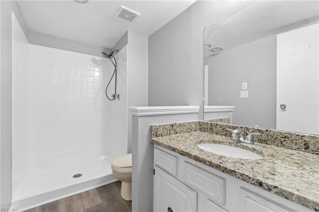 bathroom featuring vanity, hardwood / wood-style floors, toilet, and tiled shower