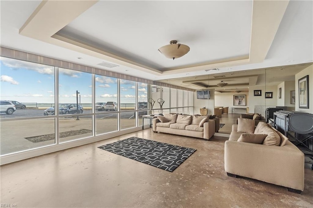 living room featuring a tray ceiling, a wall of windows, and concrete flooring