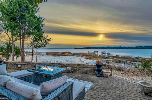 patio terrace at dusk featuring a water view and an outdoor living space with a fire pit