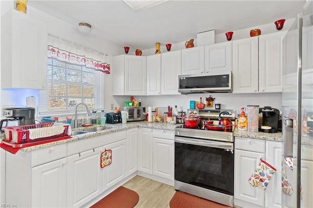 kitchen featuring sink, white cabinets, stainless steel appliances, light stone countertops, and light wood-type flooring