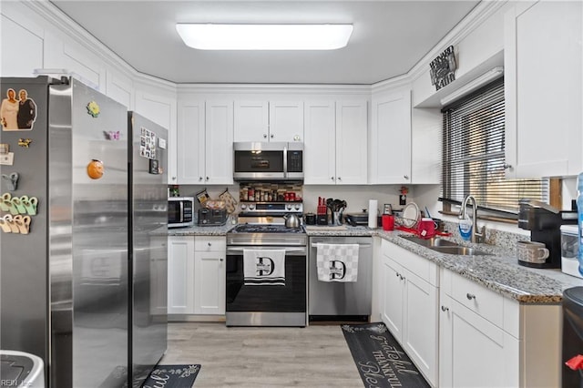 kitchen with appliances with stainless steel finishes, sink, white cabinets, light stone countertops, and light hardwood / wood-style flooring