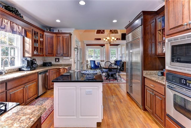 kitchen with dark stone countertops, sink, built in appliances, and a wealth of natural light