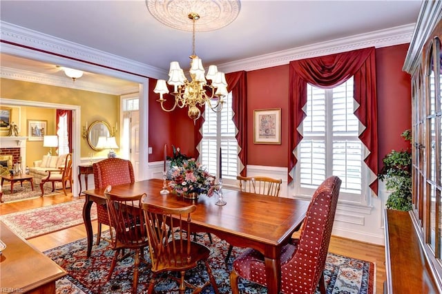 dining area with a brick fireplace, hardwood / wood-style flooring, ornamental molding, and a chandelier