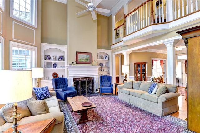 living room with built in shelves, ceiling fan, crown molding, and decorative columns