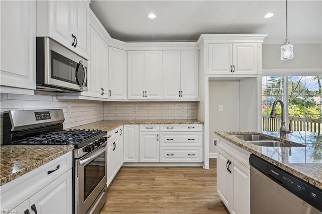 kitchen with stainless steel appliances, a sink, white cabinetry, light wood finished floors, and tasteful backsplash