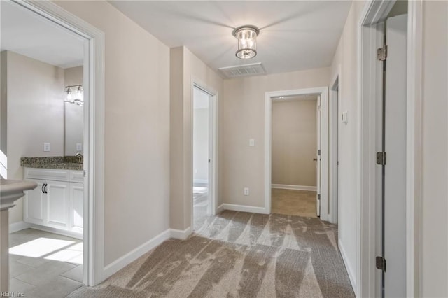 hallway featuring baseboards, visible vents, and light colored carpet