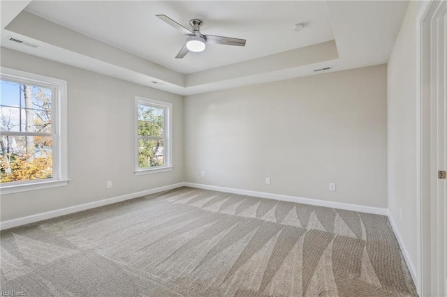 unfurnished room featuring a tray ceiling, carpet flooring, visible vents, and baseboards