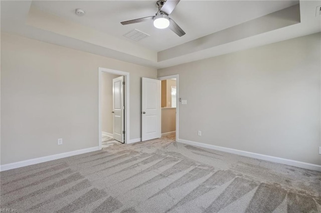 unfurnished bedroom featuring carpet, visible vents, a tray ceiling, and baseboards