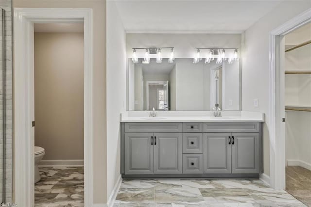 full bath with toilet, marble finish floor, double vanity, and a sink