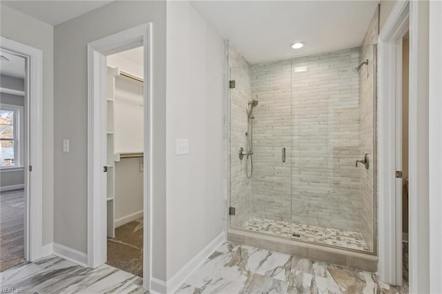 bathroom featuring a walk in closet, marble finish floor, a shower stall, and baseboards