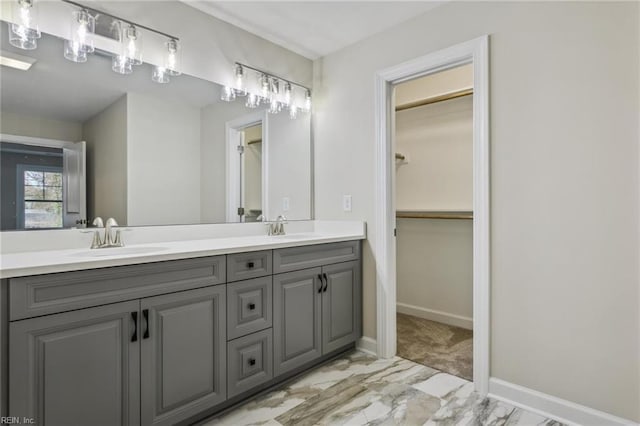 bathroom featuring double vanity, marble finish floor, baseboards, and a sink