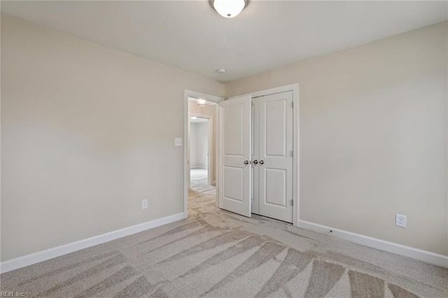 unfurnished bedroom with a closet, light colored carpet, and baseboards