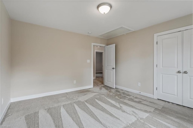 unfurnished bedroom featuring attic access, a closet, light colored carpet, and baseboards