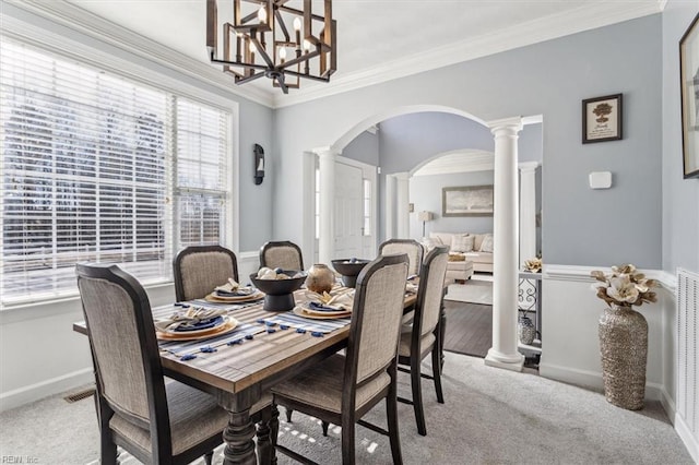 carpeted dining room featuring an inviting chandelier, ornamental molding, and ornate columns