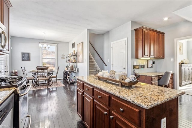 kitchen with dark wood-type flooring, hanging light fixtures, stainless steel appliances, a center island, and light stone countertops