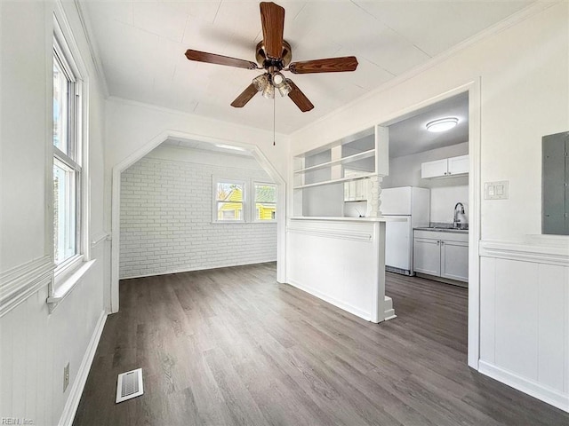 unfurnished living room featuring brick wall, sink, ceiling fan, crown molding, and dark wood-type flooring