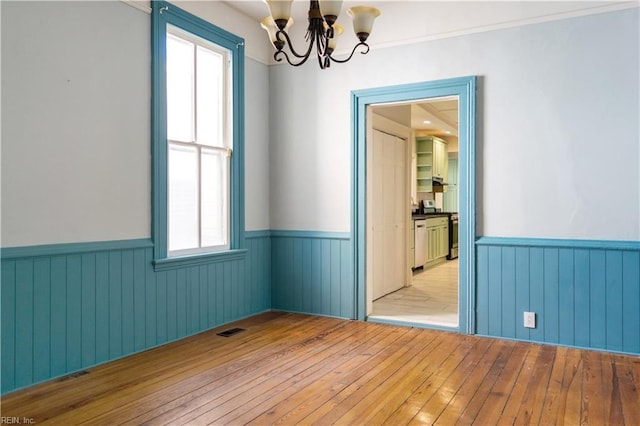 empty room with a notable chandelier, a wealth of natural light, and light wood-type flooring