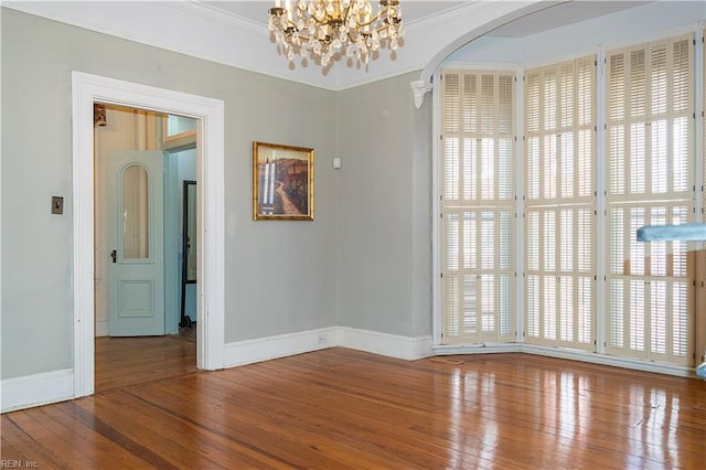 empty room with crown molding, hardwood / wood-style flooring, and an inviting chandelier