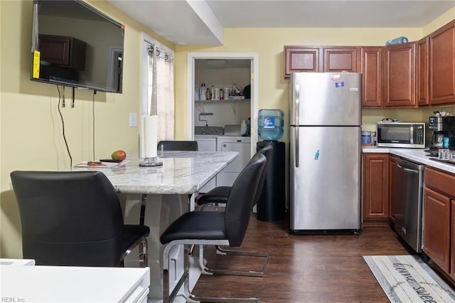 kitchen with dark wood-type flooring, appliances with stainless steel finishes, a kitchen breakfast bar, light stone countertops, and washing machine and dryer